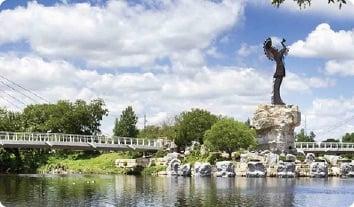 a statue on a rock in a pond with a bridge and trees