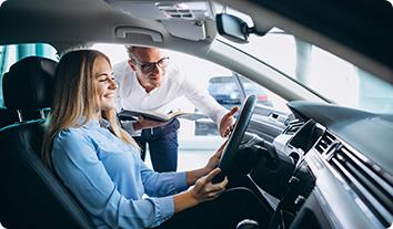 A woman sitting in the driver's seat of a car while a man is standing by the car door