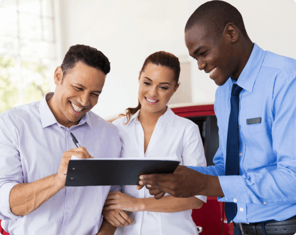 A happy couple signing paperwork on a clipboard held by a happy salesperson.