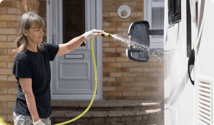 A woman washing an RV with a water hose